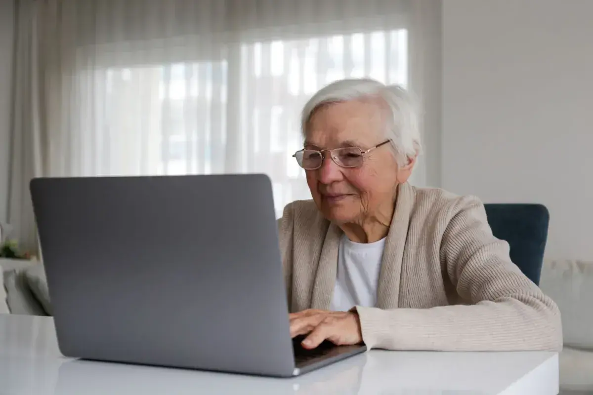 Uśmiechnięta starsza pani z okularami pracuje na laptopie, planując swoją emeryturę bez podatku.
