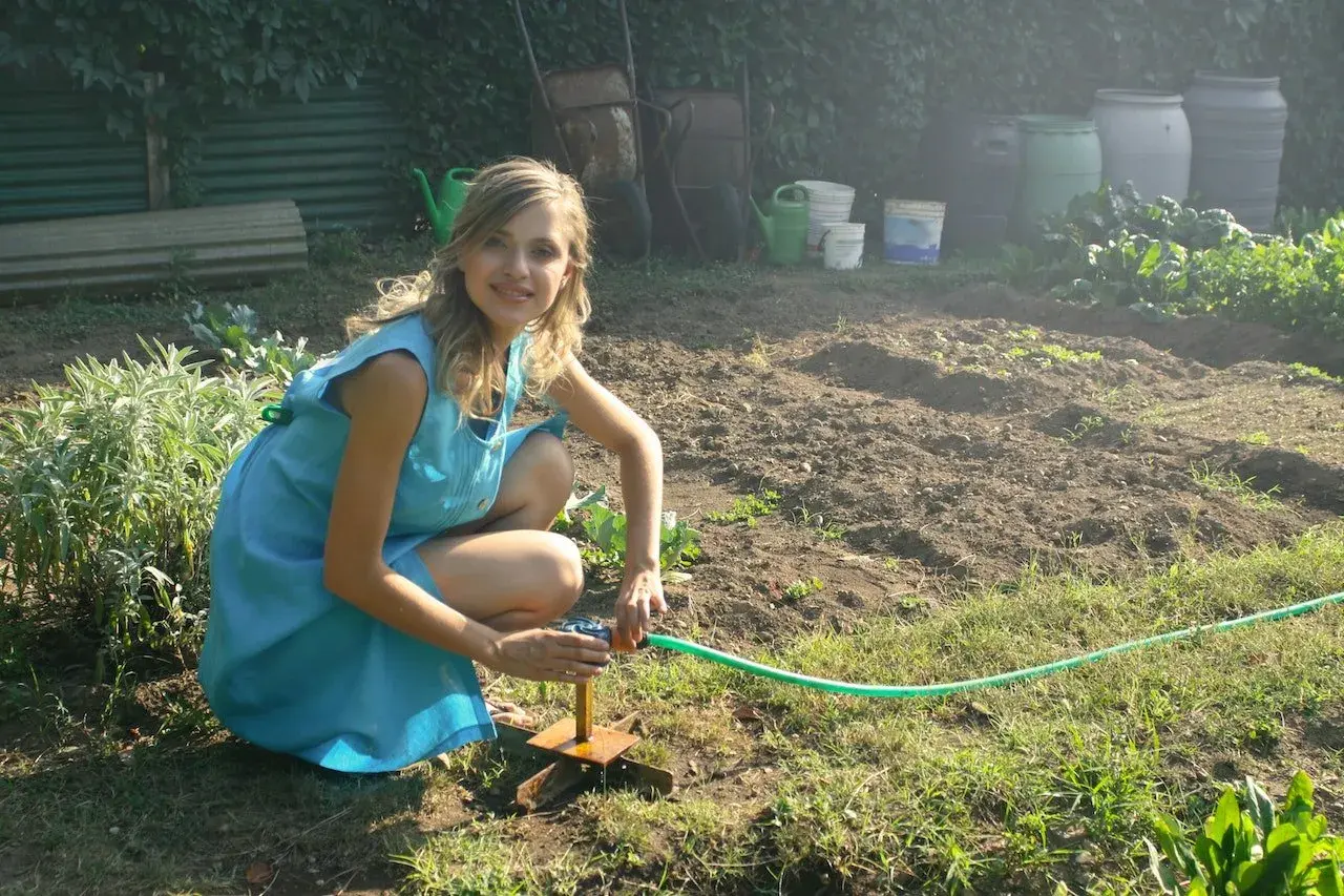 Dziewczyna w niebieskiej sukience podlewa grządki. Idealna ziemia pod uprawę jagody kamczackiej.