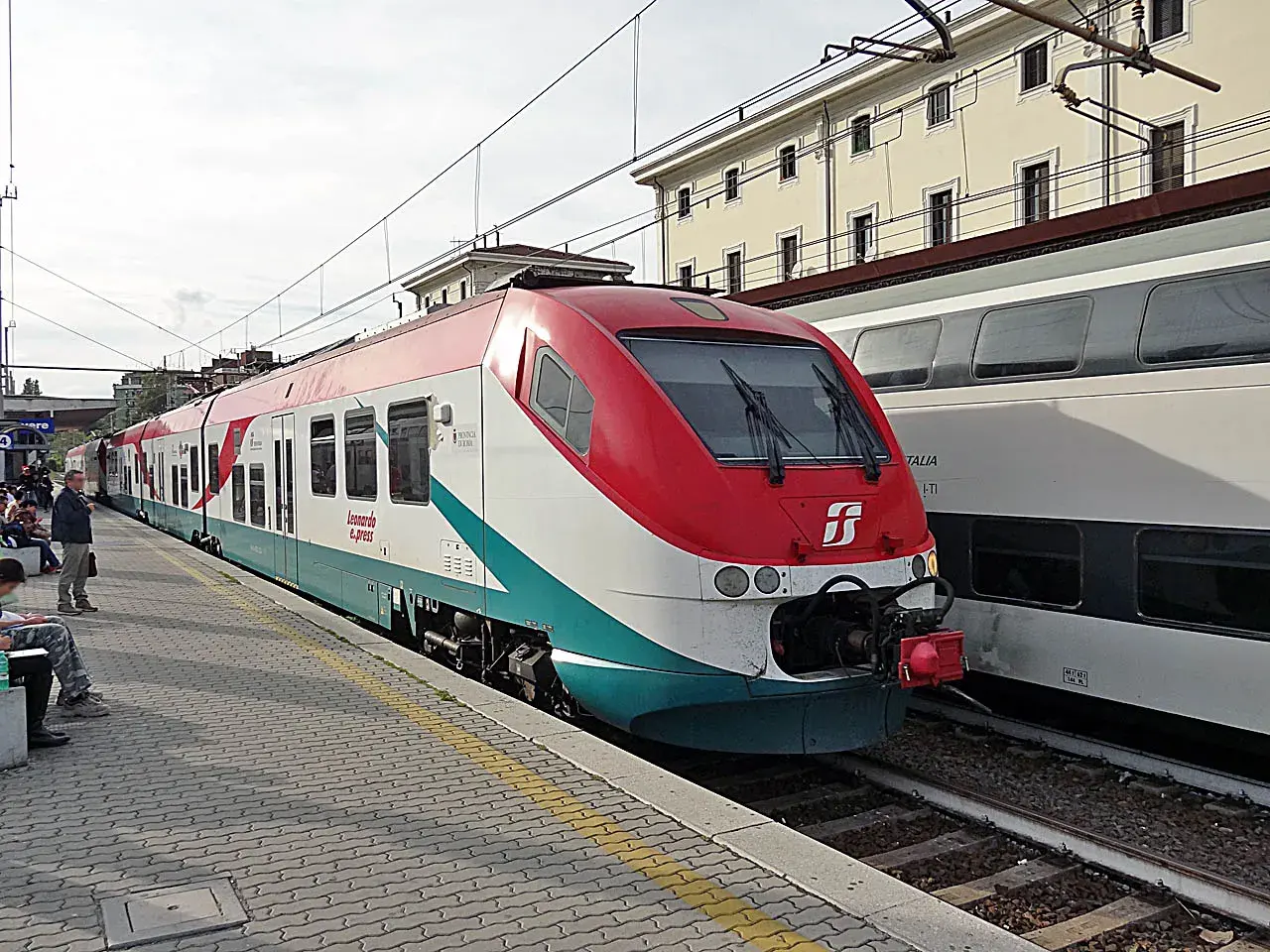 Le train Leonardo Express, reliant Fiumicino à Termini, est à quai. Des voyageurs attendent sur le quai pavé.