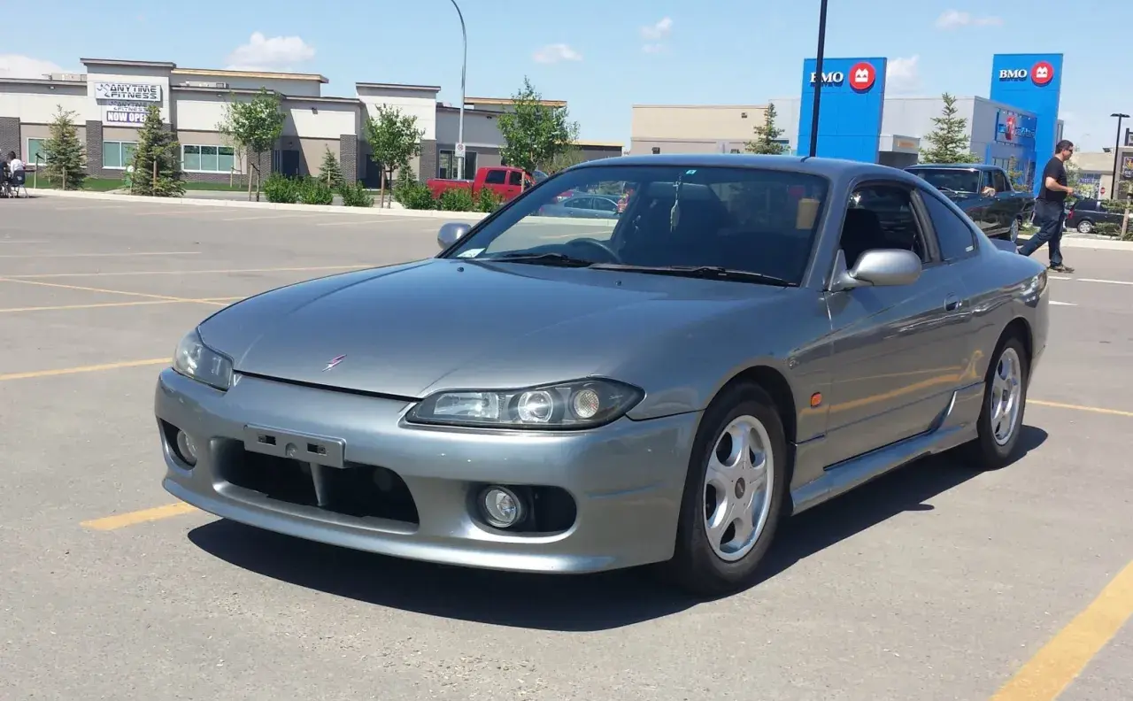 Szary Nissan Silvia s15 na parkingu przed budynkami BMO i Anytime Fitness.