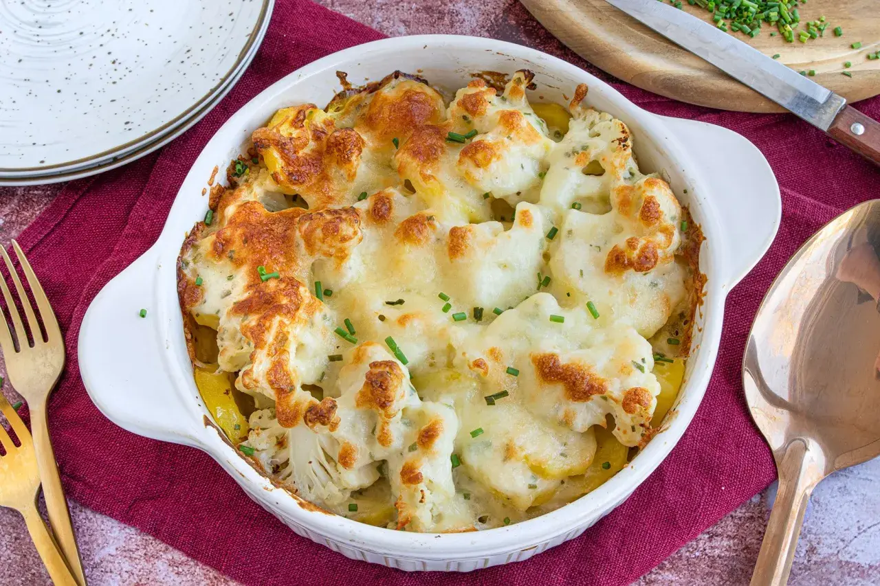 Ein goldbraun überbackener Blumenkohl Kartoffel Auflauf mit geschmolzenem Käse und frischen Kräutern, bereit zum Servieren.