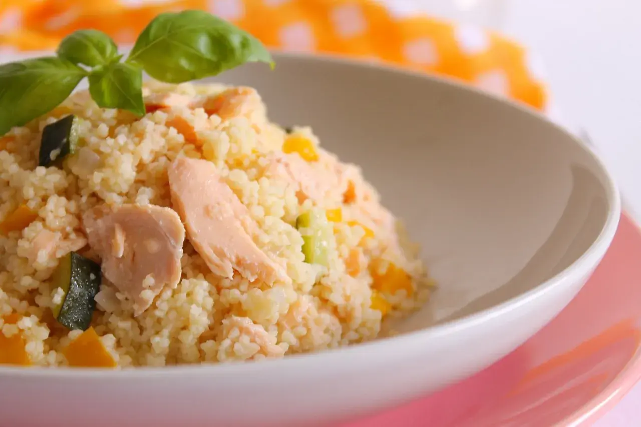 Un gustoso cous cous con salmone, zucchine e peperoni, condito con un tocco di salsa di soia e guarnito con basilico fresco.