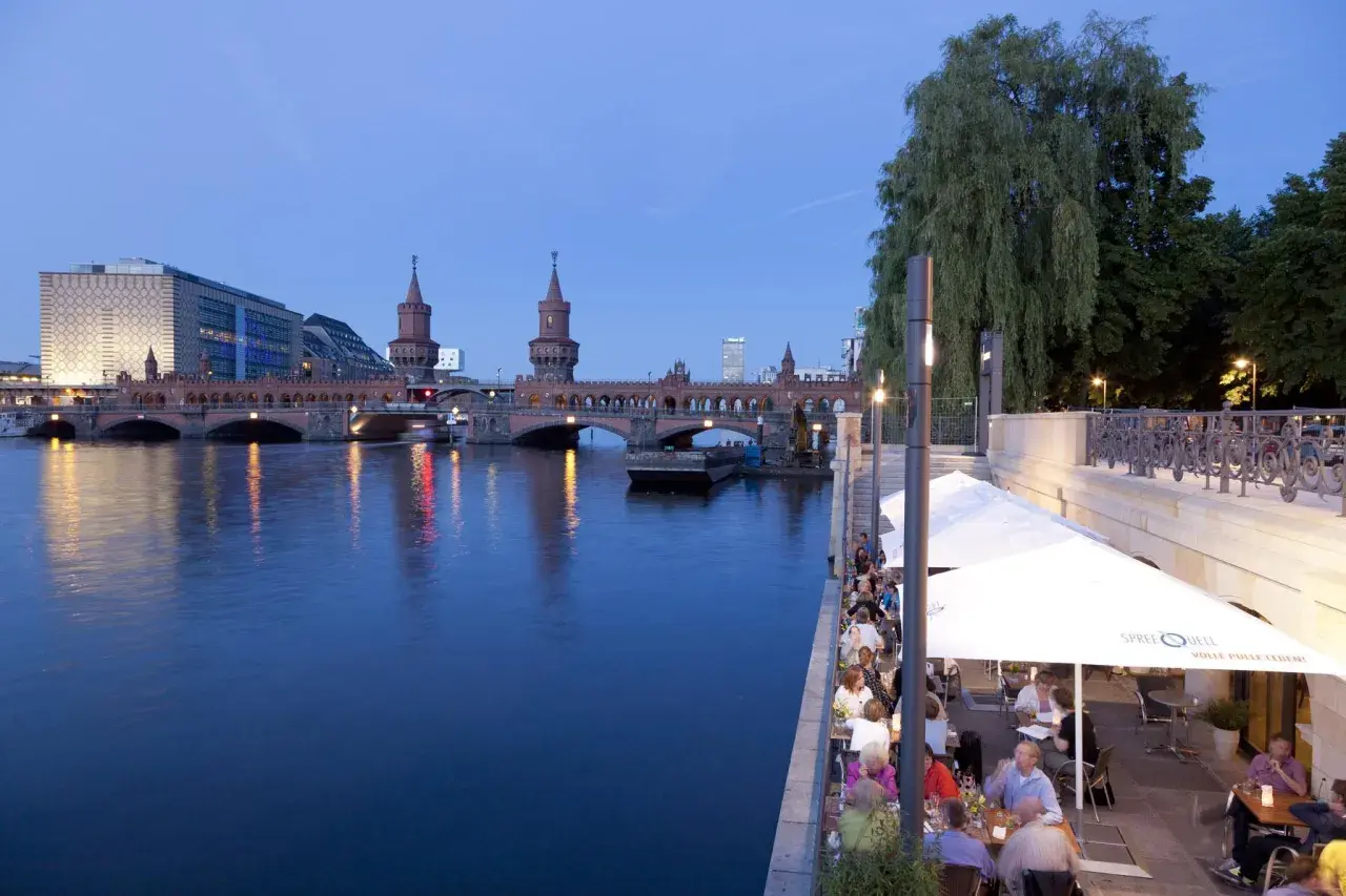Abendstimmung an den Rivo SpreeTerrassen: Gäste genießen das Ambiente am Wasser mit Blick auf die Oberbaumbrücke.