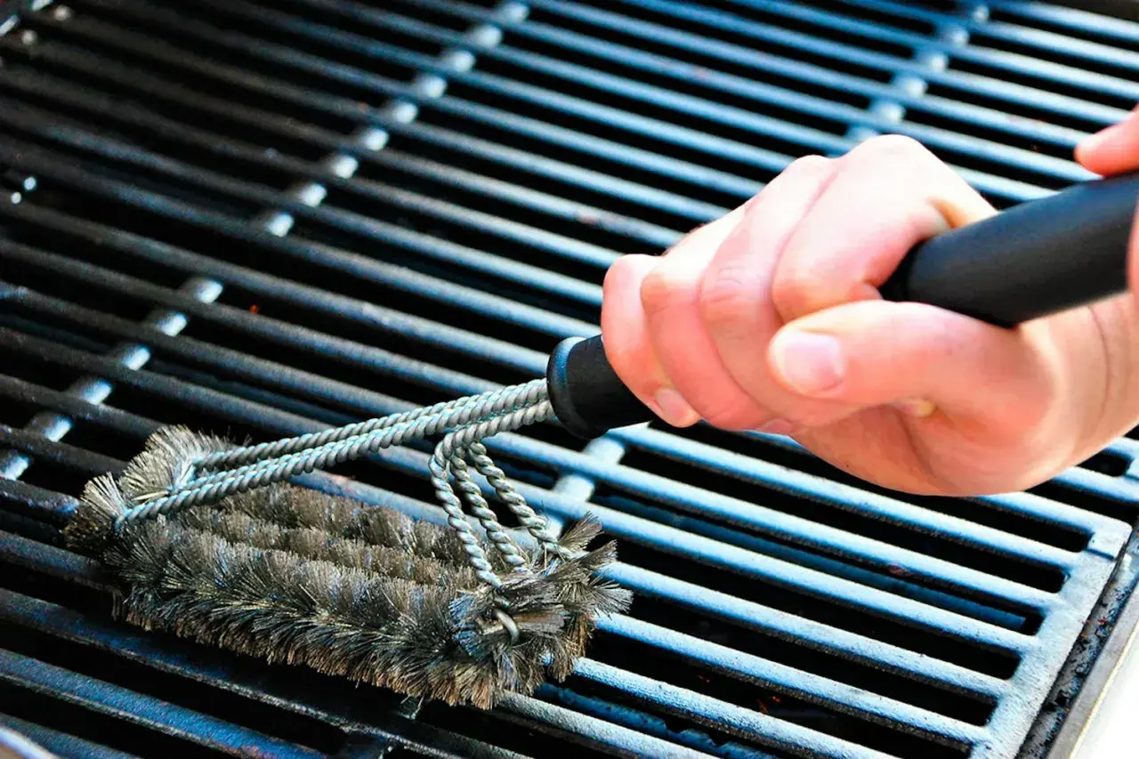 En hand använder en grillborste för att rengöra grillen. Avfettning behövs för att få bort envis smuts.