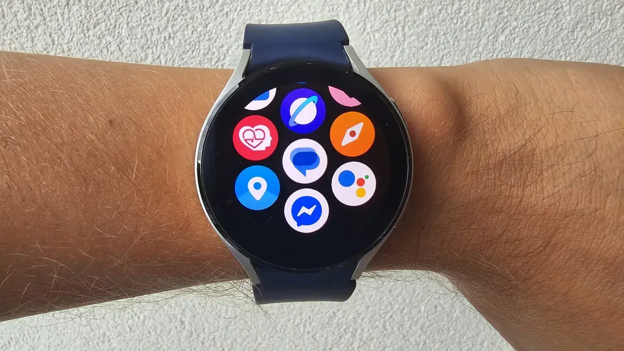 Zegarek z systemem Wear OS na nadgarstku, z widocznymi ikonami aplikacji: serce, lokalizacja, Messenger, Google Assistant i inne.