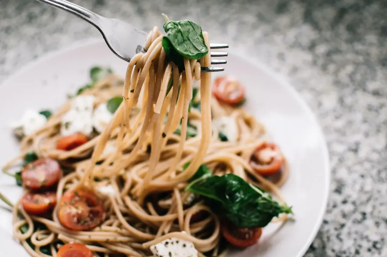 Widok z bliska na makaron z pesto ze słoika i śmietaną, z pomidorkami koktajlowymi i mozzarellą.
