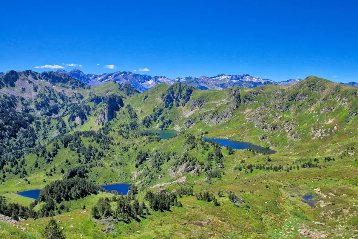 Vue panoramique sur les Pyrénées avec plusieurs étangs bleus, dont l'étang de Rabassoles, nichés dans des vallées verdoyantes sous un ciel bleu intense.