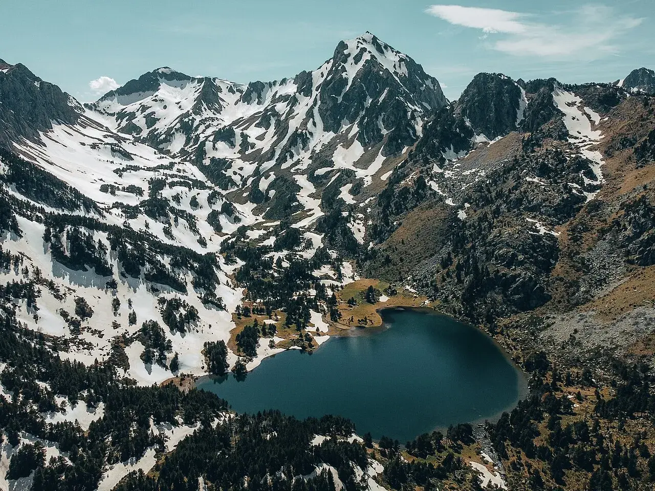 Vue aérienne du lac du Laurenti, niché au pied de montagnes enneigées et de forêts de pins. Un paysage alpin spectaculaire.