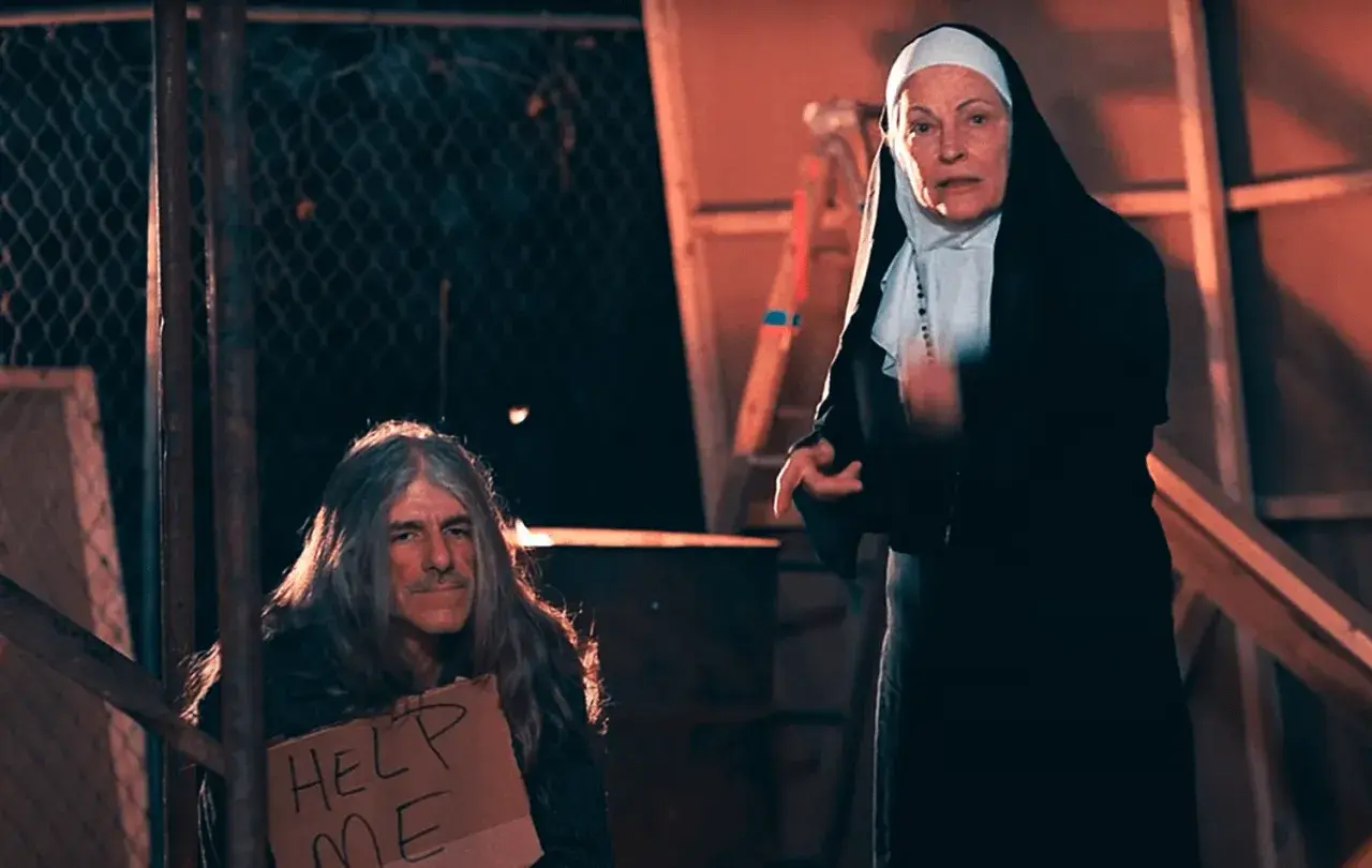 Una monja mira a un hombre con pelo largo y un cartel de "Ayúdame". Podría ser una escena de un sueño con monjas.
