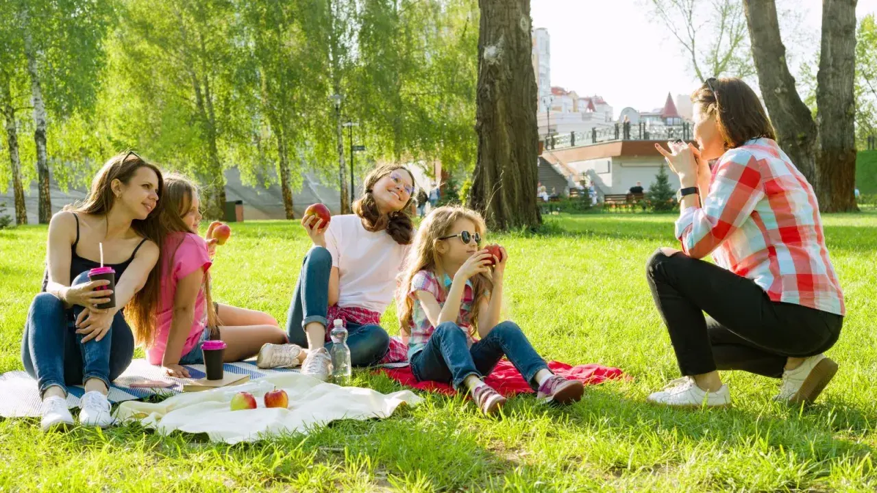 Rodzina na pikniku w parku. Czy Boże Ciało jest dniem wolnym od pracy? Dzieci jedzą jabłka, ciesząc się słońcem.
