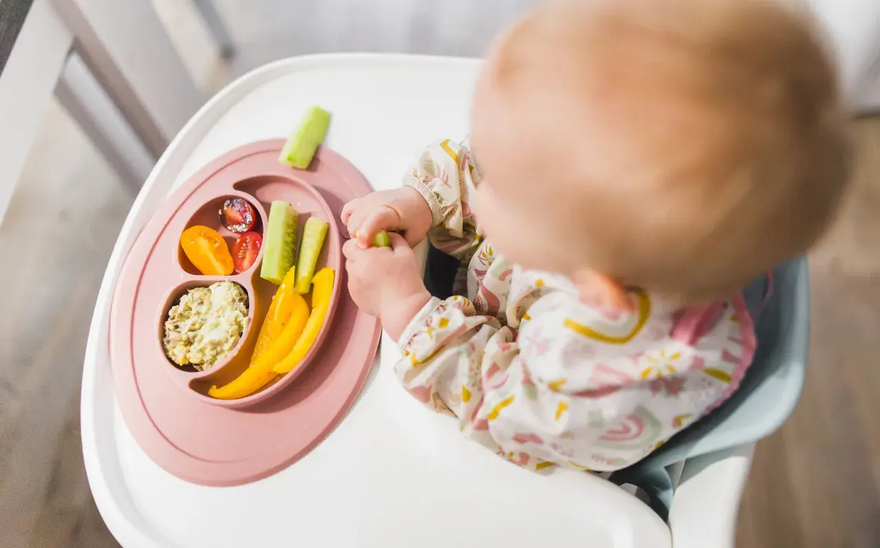 Dziecko odkrywa smaki warzyw, stosując metodę blw. Na talerzyku: pomidorki, ogórek, papryka i pasta.