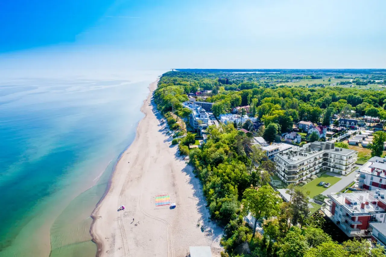 Idealny pobyt nad morzem: piaszczysta plaża, turkusowa woda i nowoczesne apartamenty wśród zieleni.