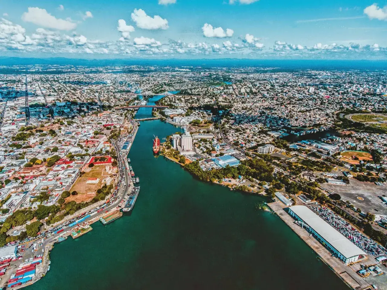 Luftaufnahme der Stadt mit einem Fluss, der sich durch sie schlängelt. Hier ist, wo Santo Domingo liegt, mit Schiffen im Hafen und vielen Gebäuden.