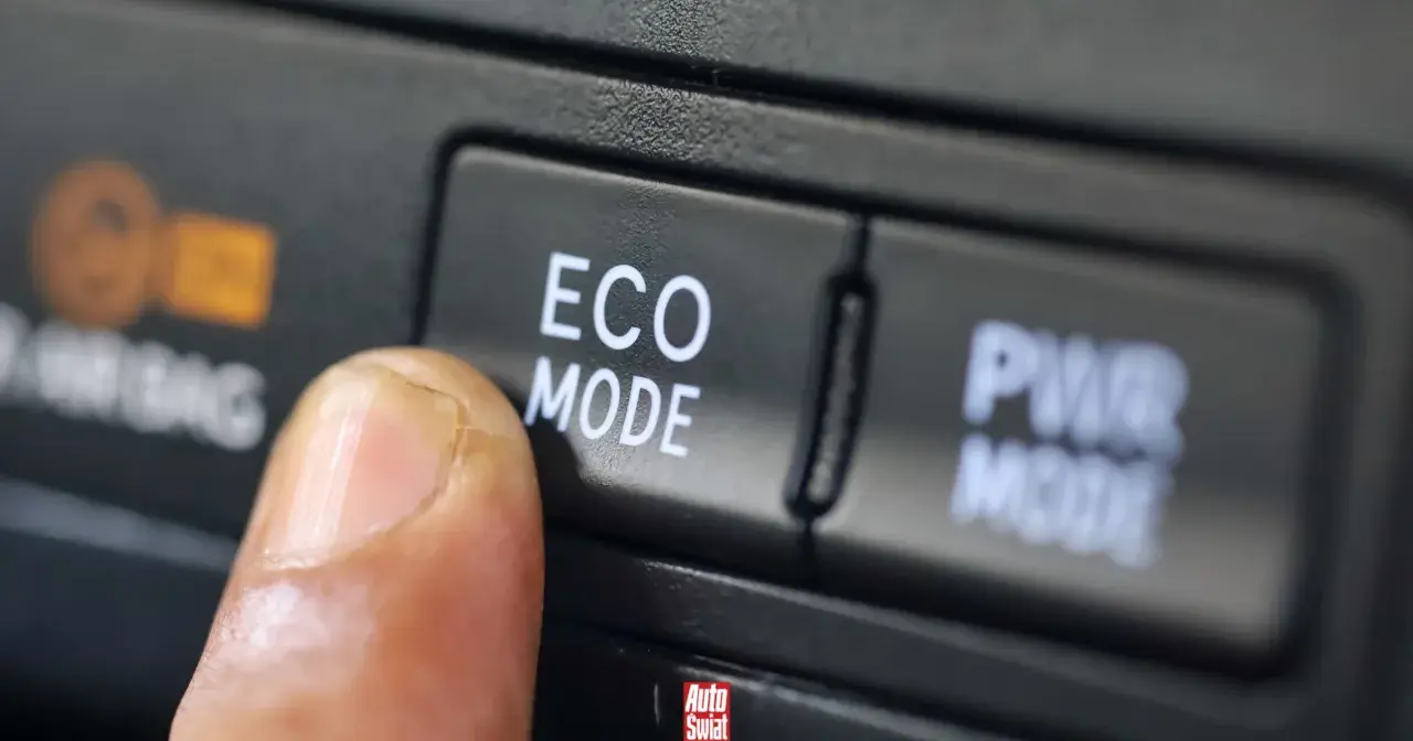 Palec naciska przycisk "ECO MODE", pytając "econ co to?". Obok przycisk "PWR MODE".