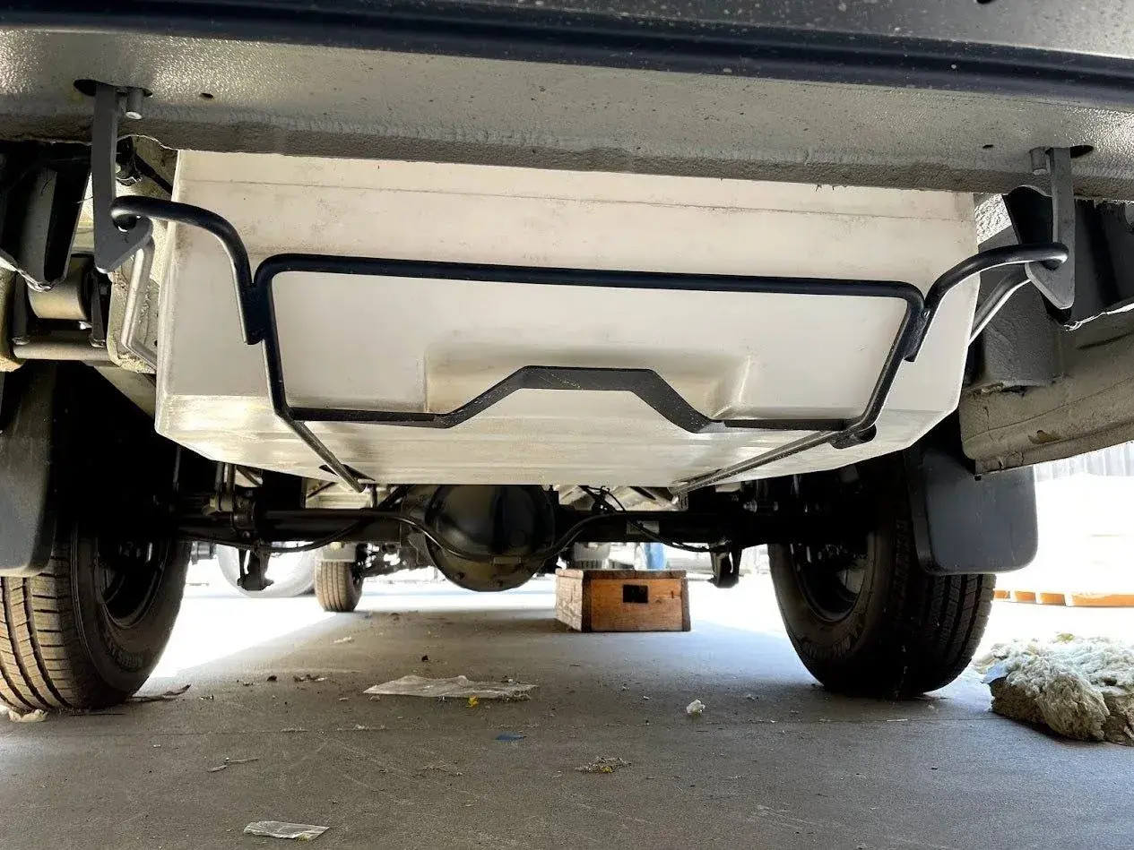 Vue sous un camping-car, montrant le réservoir d'eau propre fixé au châssis. Préparation pour le nettoyage de la cuve camping car.