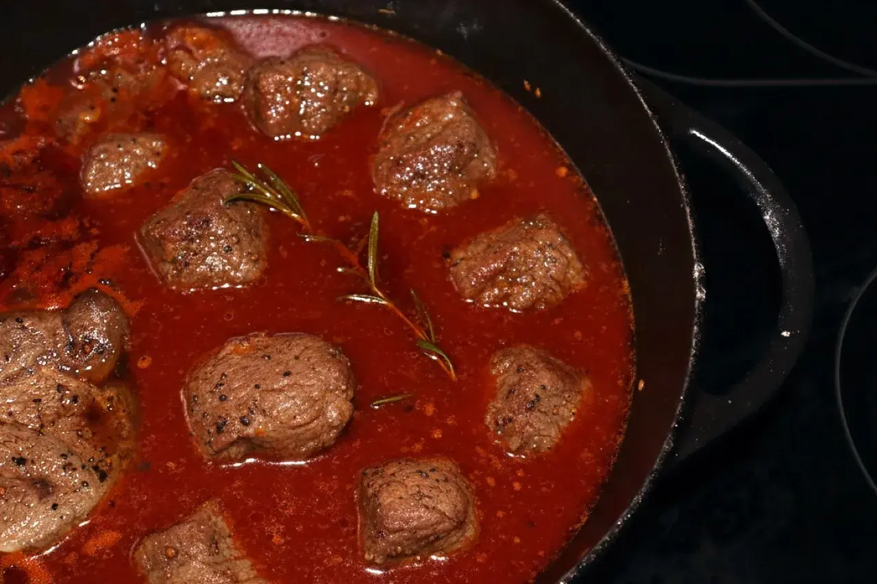 Stracotto di manzo schmort in einer tiefroten Sauce mit Rosmarin. Zarte Fleischstücke, perfekt für ein herzhaftes Gericht.