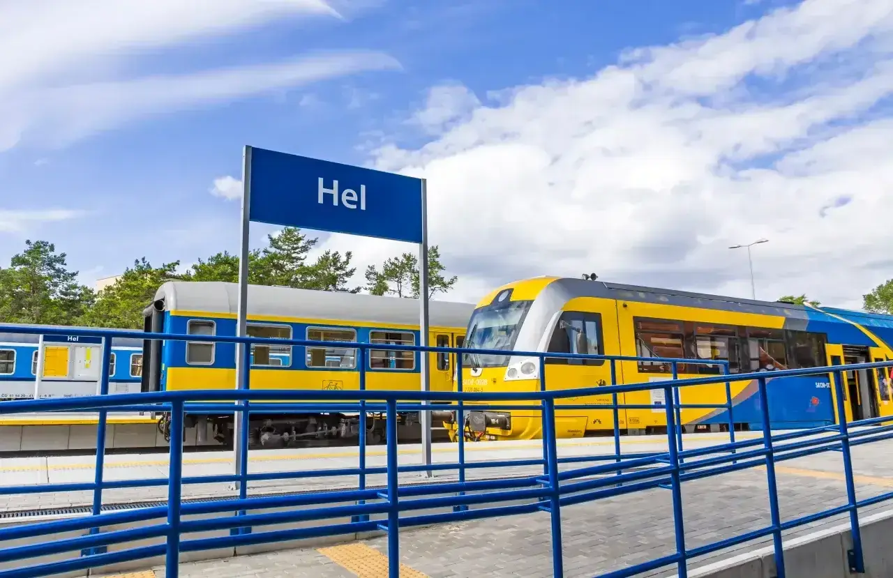 Pociąg z Władysławowa do Helu stoi na stacji. Żółto-niebieskie wagony czekają na pasażerów.