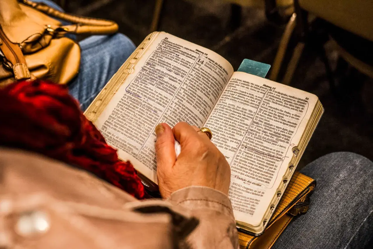 Osoba czyta Biblię, skupiając się na psalm 9. W tle widać torebkę i fragmenty ubrania.