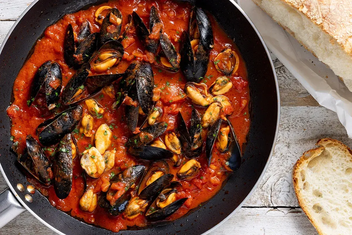 Cozze alla tarantina in padella, un piatto ricco di sapore con cozze succulente in salsa di pomodoro, accompagnate da pane fresco.