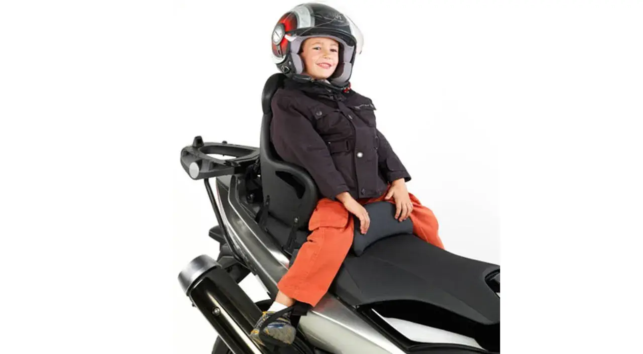 Niño sonriente con casco en asiento de moto. ¿A qué edad puede ir un niño en moto? Depende de la normativa y el equipo.