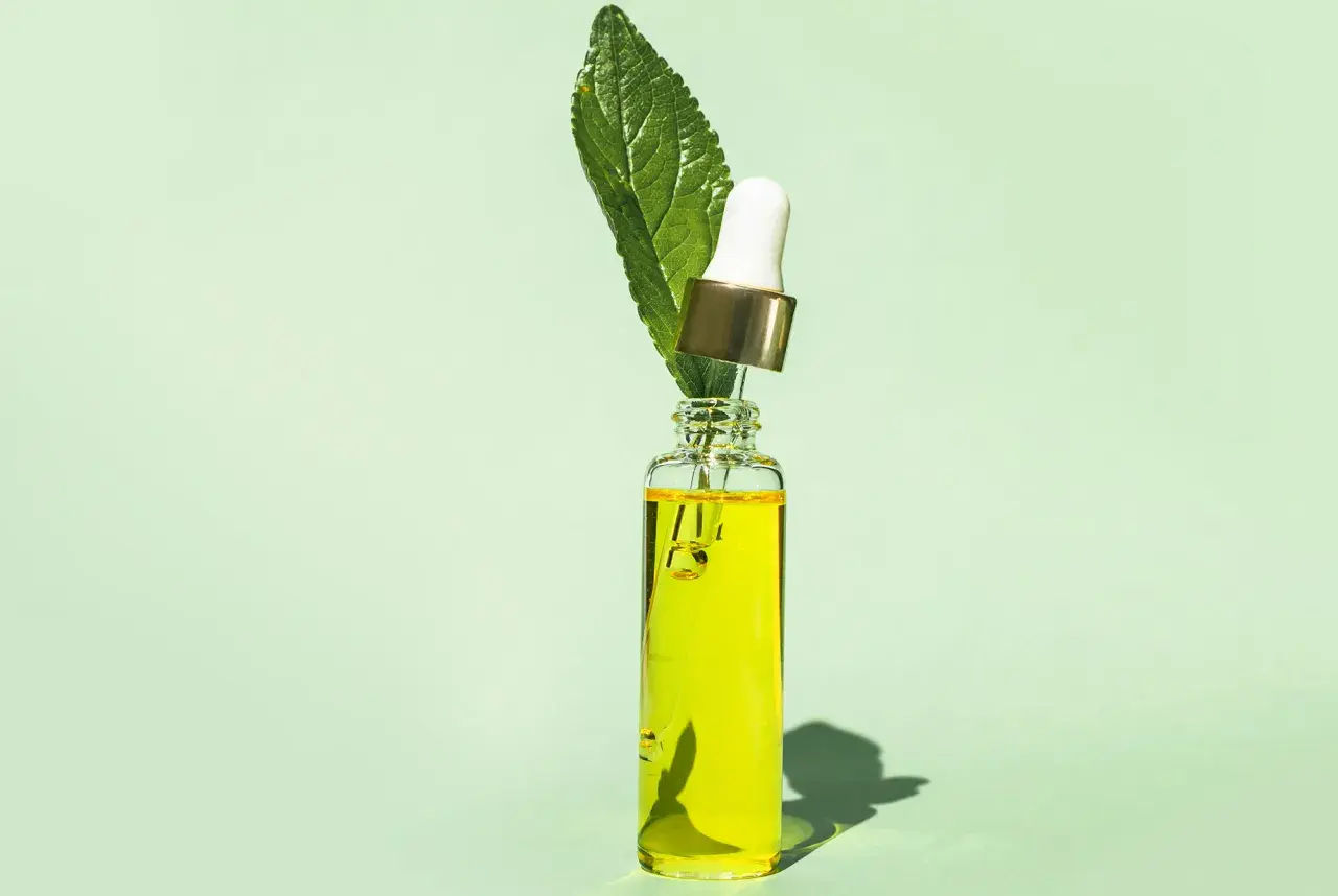 En droppe av ren tee tree oil i en glasflaska med en grön blomma.
