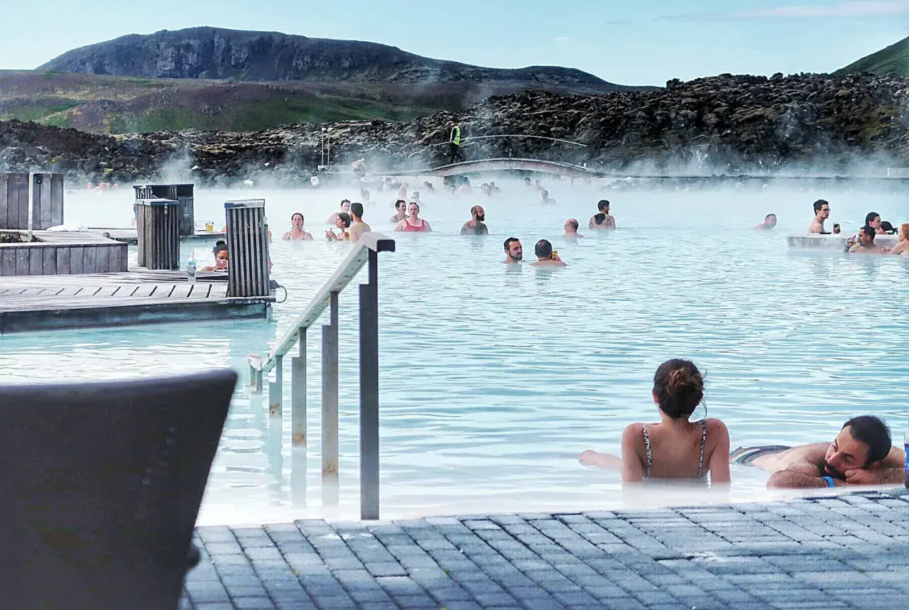Ludzie relaksują się w turkusowej wodzie Blue Lagoon, otoczeni parującym krajobrazem i skalistymi wzgórzami.