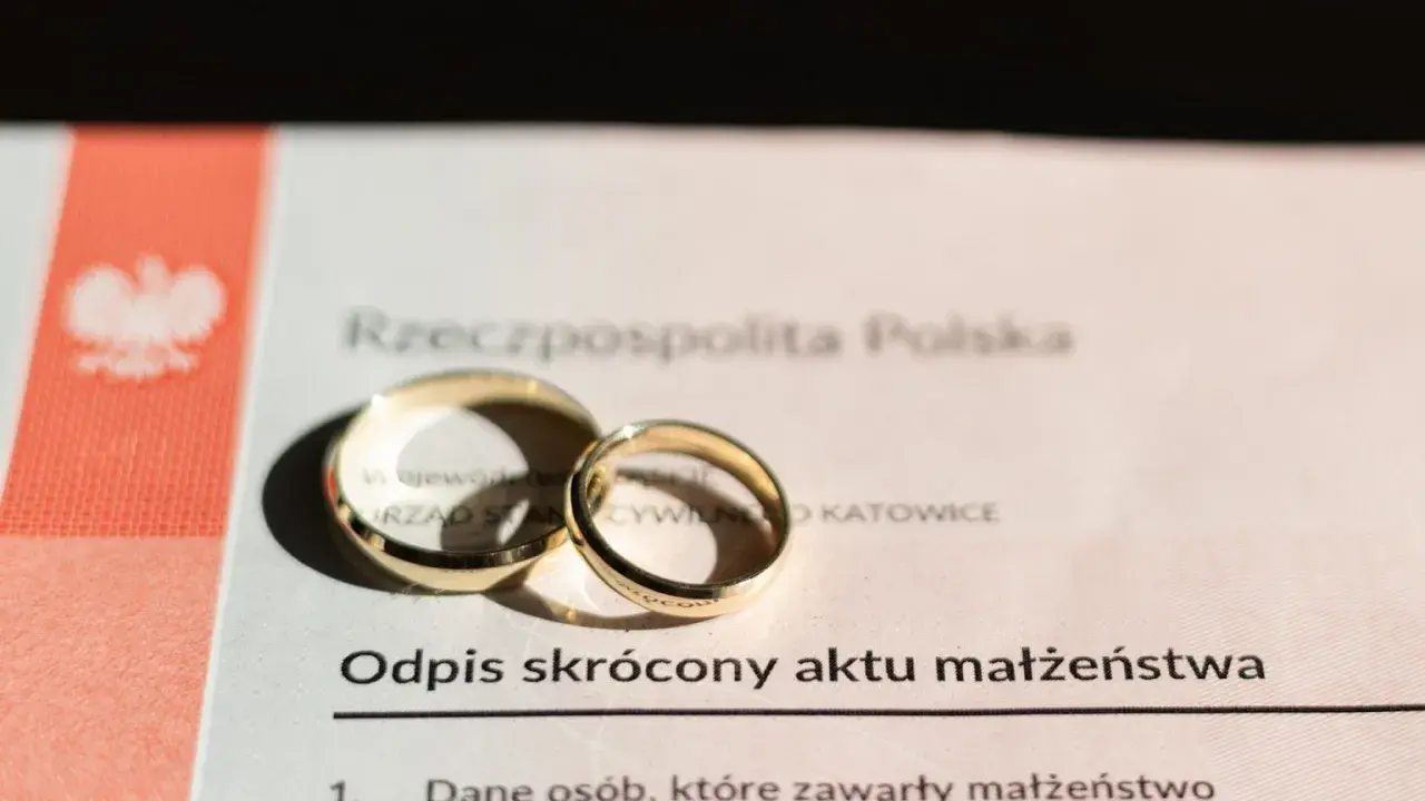 Złote obrączki na odpisie skróconym aktu małżeństwa, symbolizujące związek.
