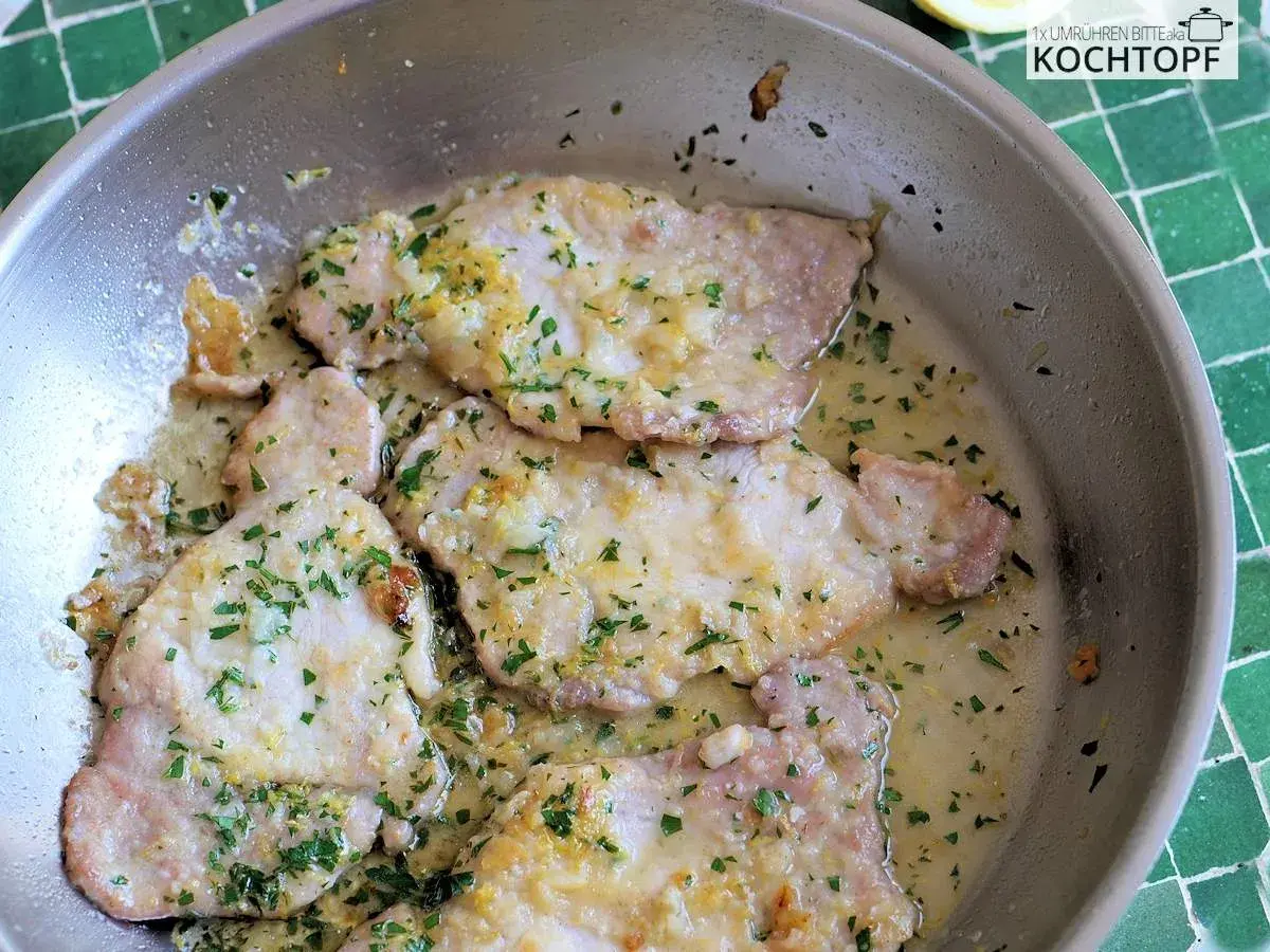 Zarte Scaloppine al Limone in einer Pfanne, garniert mit frischer Petersilie und Zitronenschale. Ein Klassiker der italienischen Küche.