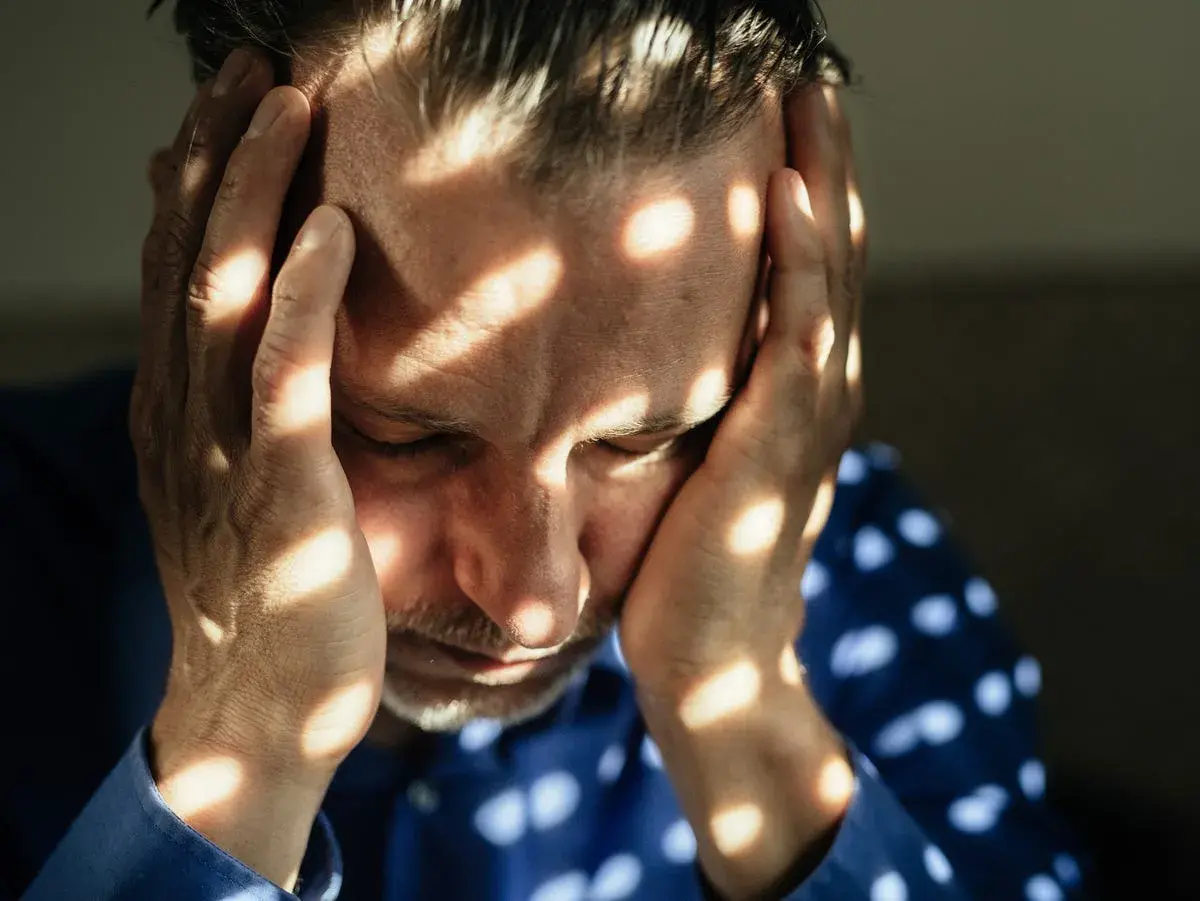 Uomo con le mani sulla testa, illuminato da fasci di luce che creano un effetto di **blocco emotivo test**.