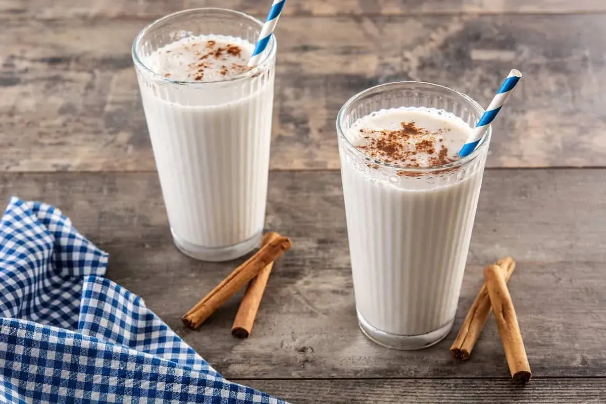 Dos vasos de horchata, bebida refrescante de chufa con canela, sobre mesa de madera.