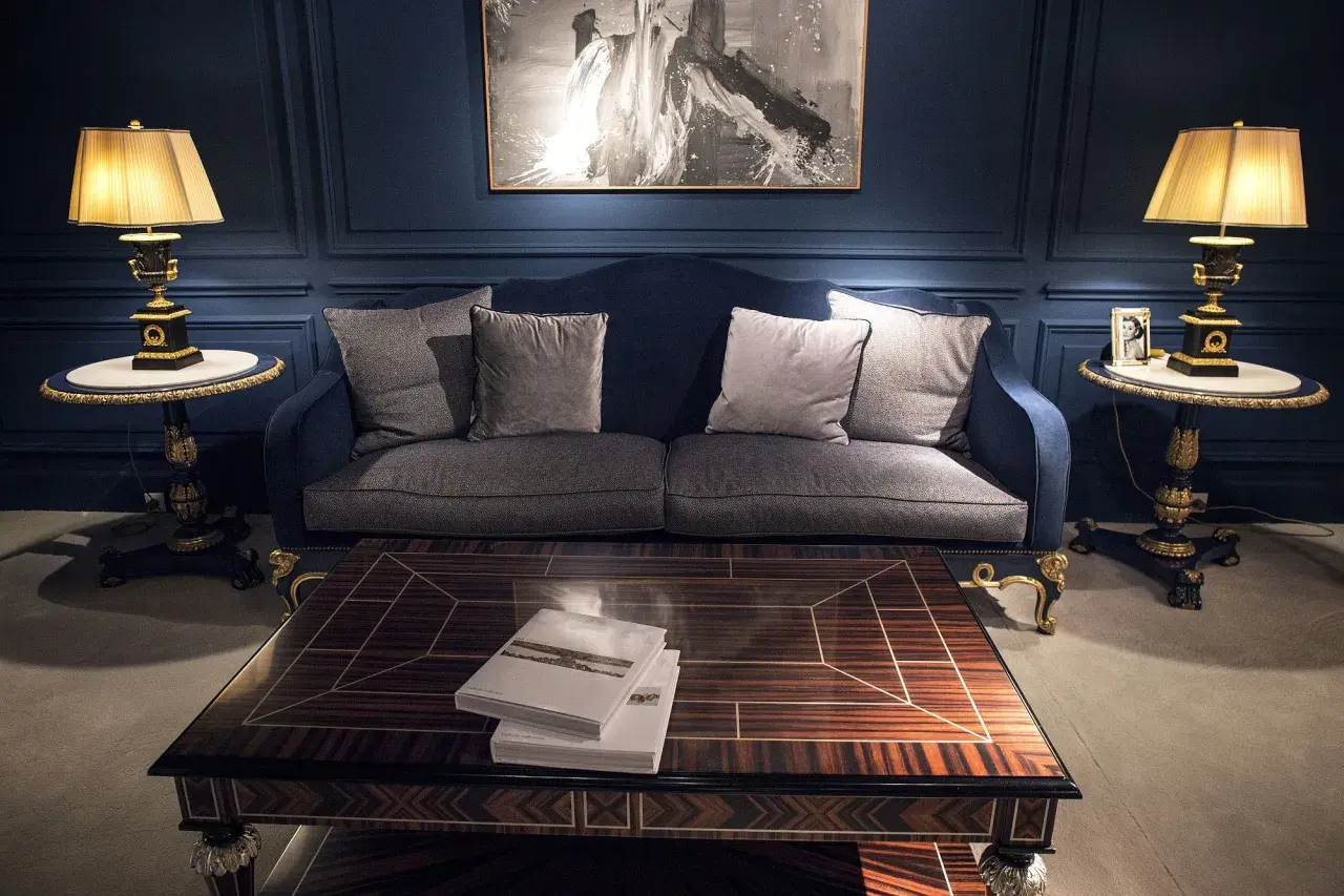 Elegante salón con sofá azul, mesa de centro de madera y dos lámparas de mesa clásicas doradas.
