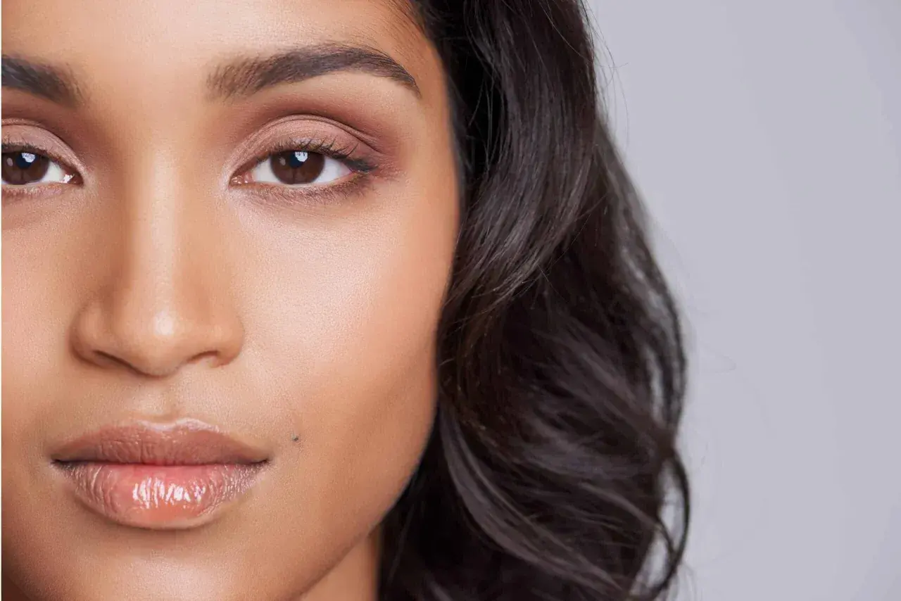 Un grain de beauté discret, comme un petit tatouage naturel, orne la joue d'une jeune femme aux yeux expressifs et aux lèvres brillantes.