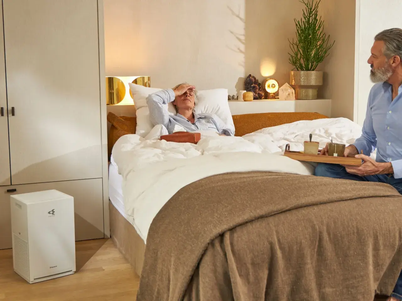 Hombre cuida a mujer enferma en cama. Purificador de aire Daikin al lado, mejorando la calidad del aire iaq.