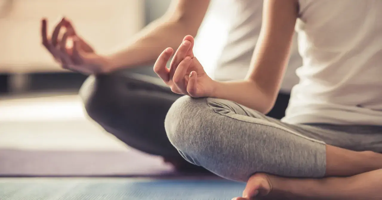 Zwei Personen in entspannter Haltung, Hände in Mudras. Eine friedliche Szene, die Entspannungstechniken bei Stress zeigt.