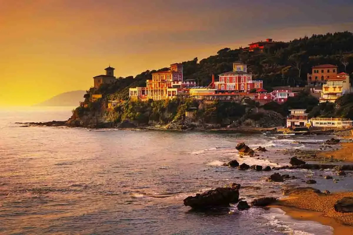 Ville colorate aggrappate alla scogliera, con il mare che lambisce la costa rocciosa. Un tramonto dorato illumina i borghi vicino Castiglioncello.