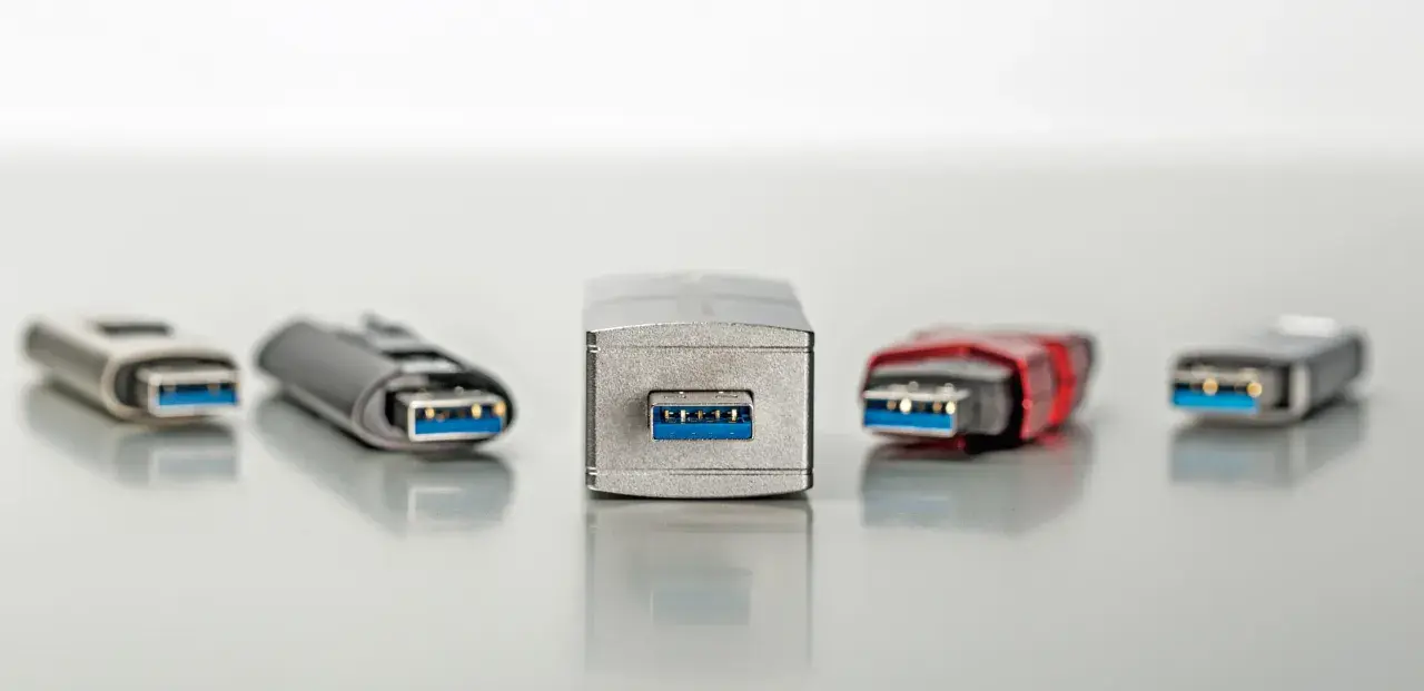 Fünf USB-Sticks in verschiedenen Designs, alle mit blauem Anschluss. Einer davon, der mittlere, wirkt besonders robust, fast wie ein Relikt aus der Zeit der USB 1.0 Geschwindigkeit.