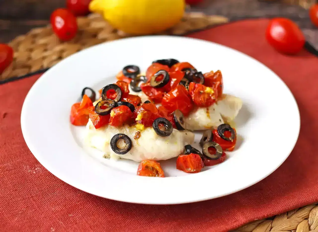 Delizioso merluzzo in friggitrice ad aria, condito con pomodorini e olive nere, pronto per essere gustato.