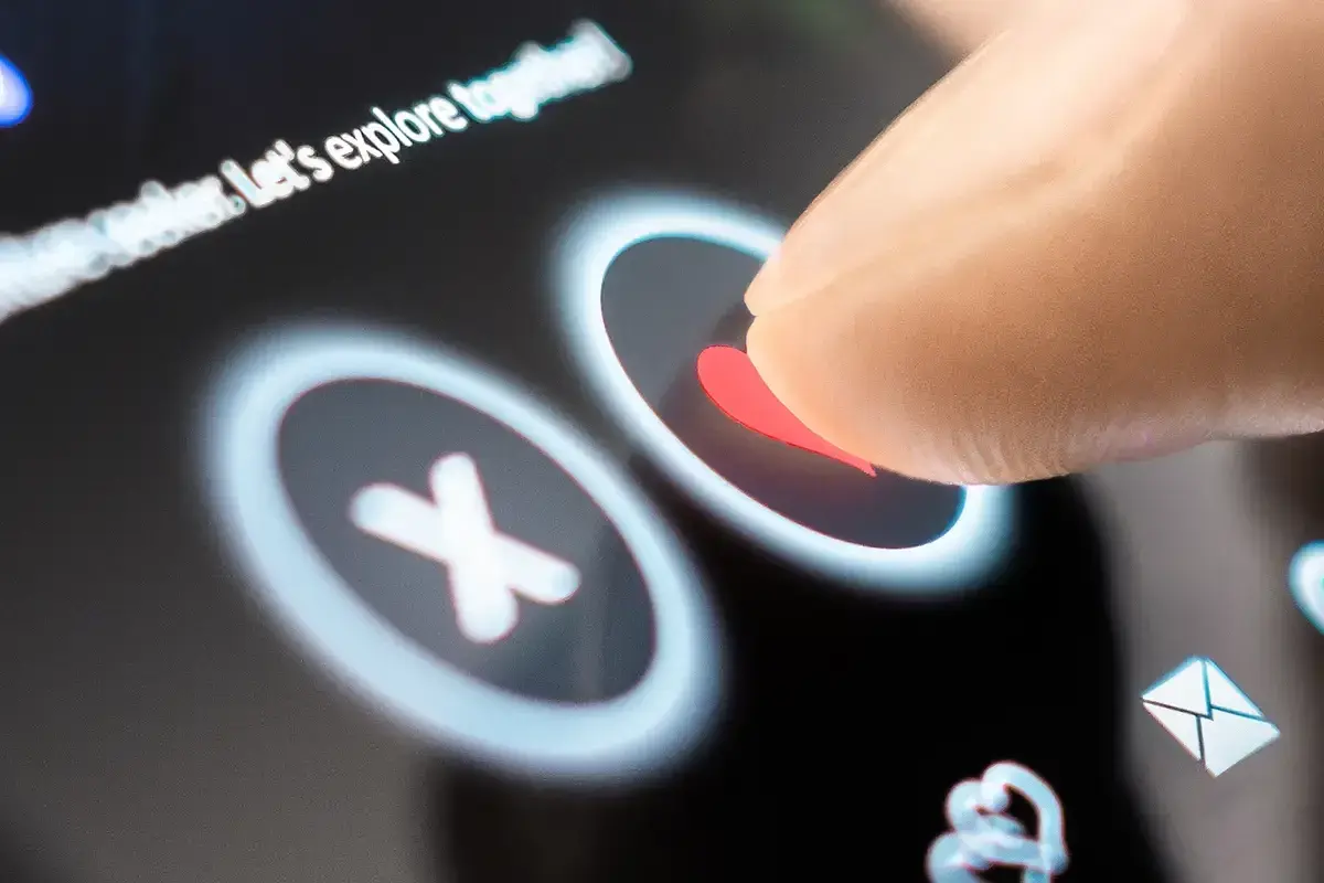 Palec dotyka serca na ekranie telefonu, wybierając potencjalną randkę. Aplikacje randkowe na telefon ułatwiają poznawanie nowych ludzi.