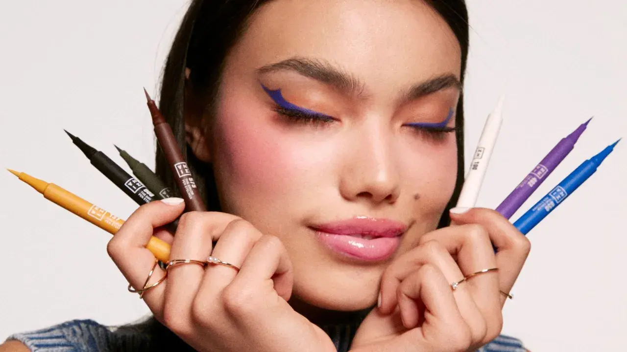 Mujer con delineado azul vibrante y varios eyeliners de colores en sus manos. Descubre qué es el eyeliner perfecto para ti.