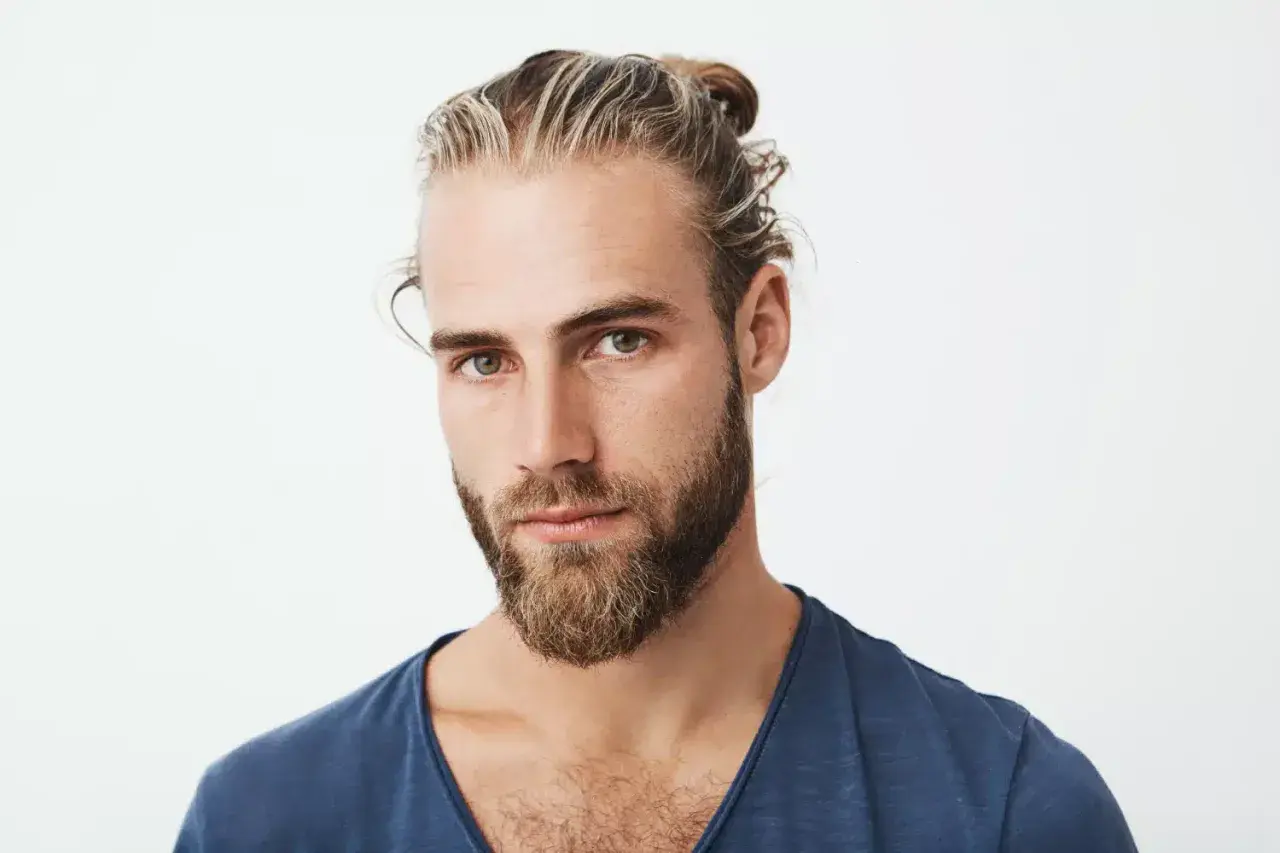 Hombre con barba y moño, luciendo unas modernas mechas rubias que resaltan su estilo.