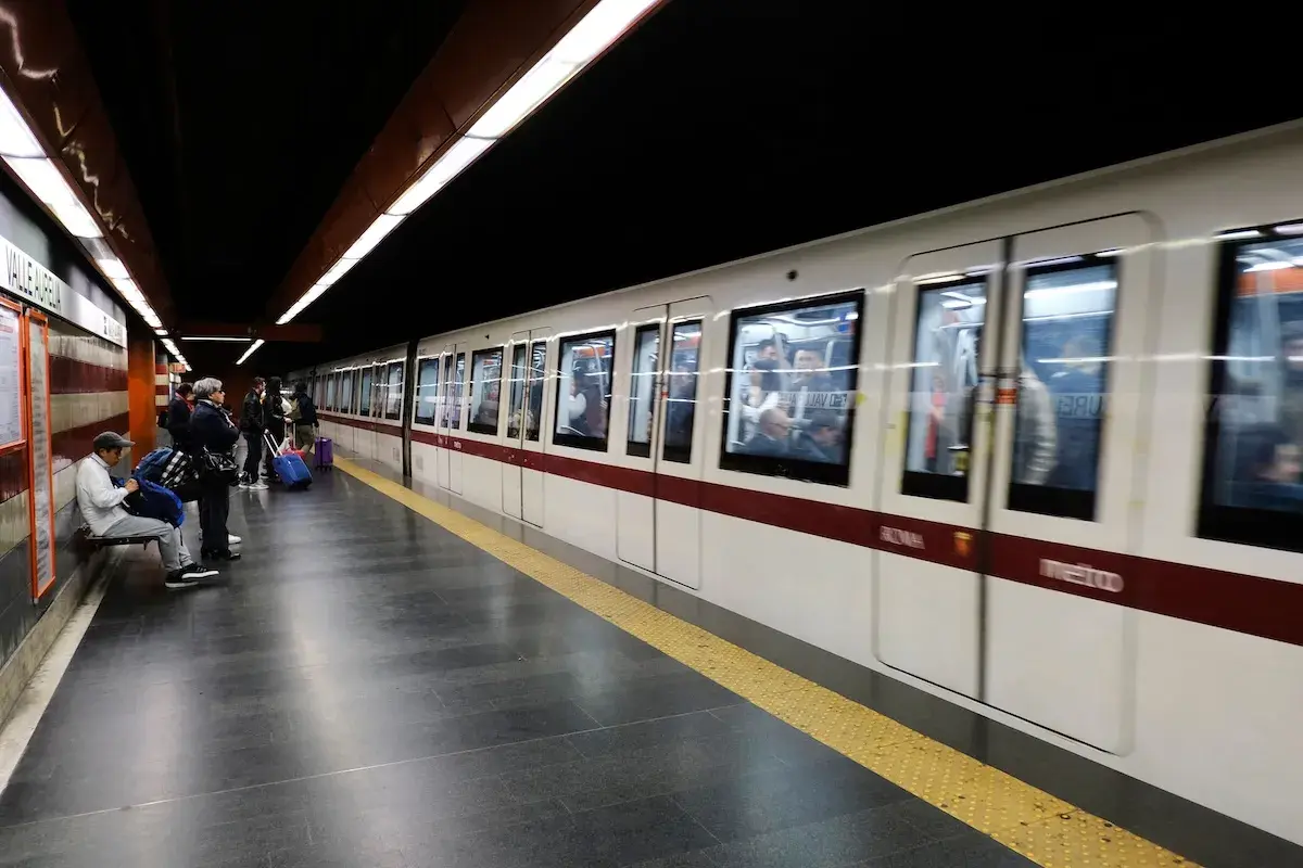 Des voyageurs attendent sur le quai du **metro a Rome**. Un train blanc et bordeaux arrive, reflétant les lumières du tunnel.