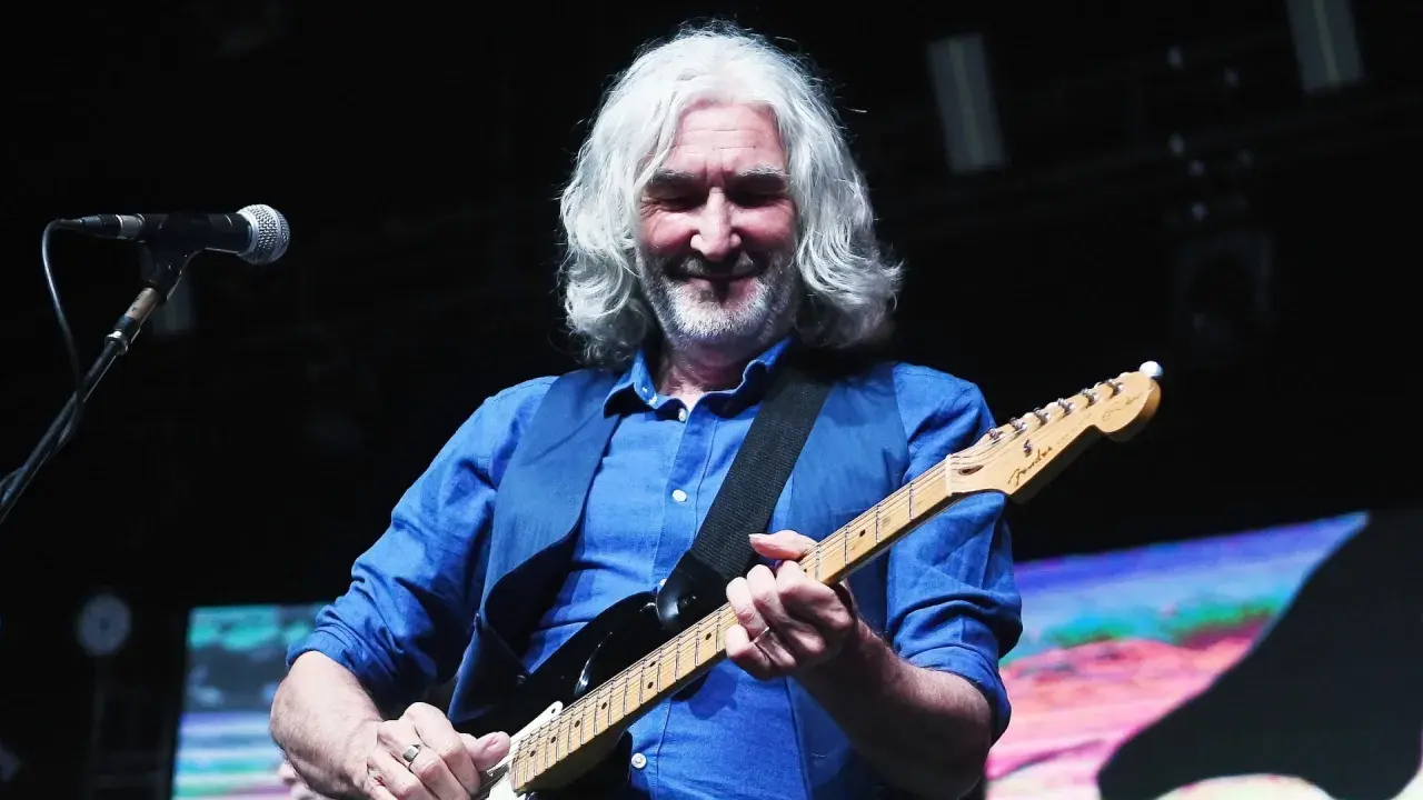 Muzyk z siwymi włosami gra na gitarze, przypominając legendarne utwory Dire Straits.
