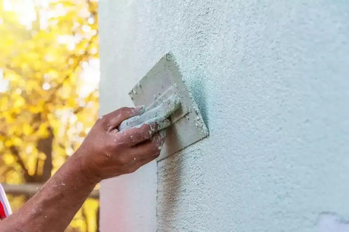 Ręka fachowca wygładza świeży tynk gąbką. Gąbkowanie tynku po jakim czasie daje najlepszy efekt?