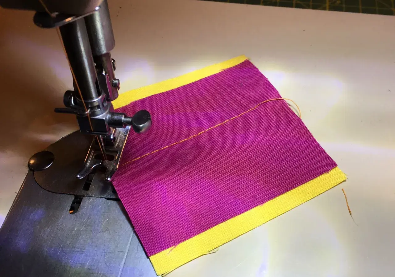 Close-up of a sewing machine needle and foot over purple fabric with a yellow border, demonstrating how to thread a sewing machine.