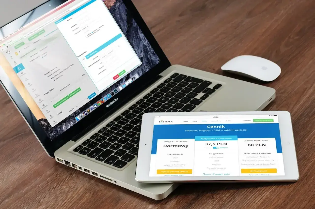 Programista .NET pracuje nad aplikacją na laptopie i tablecie. Na ekranach widoczne są formularze i cennik usług.