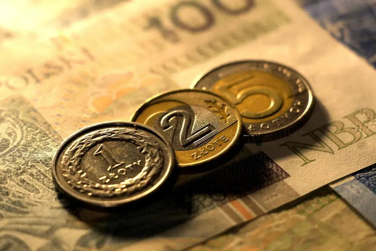 Monety 1, 2 i 5 złotych na tle banknotu 100 zł. Zastanawiasz się, przedterminowy wykup obligacji ile trwa?