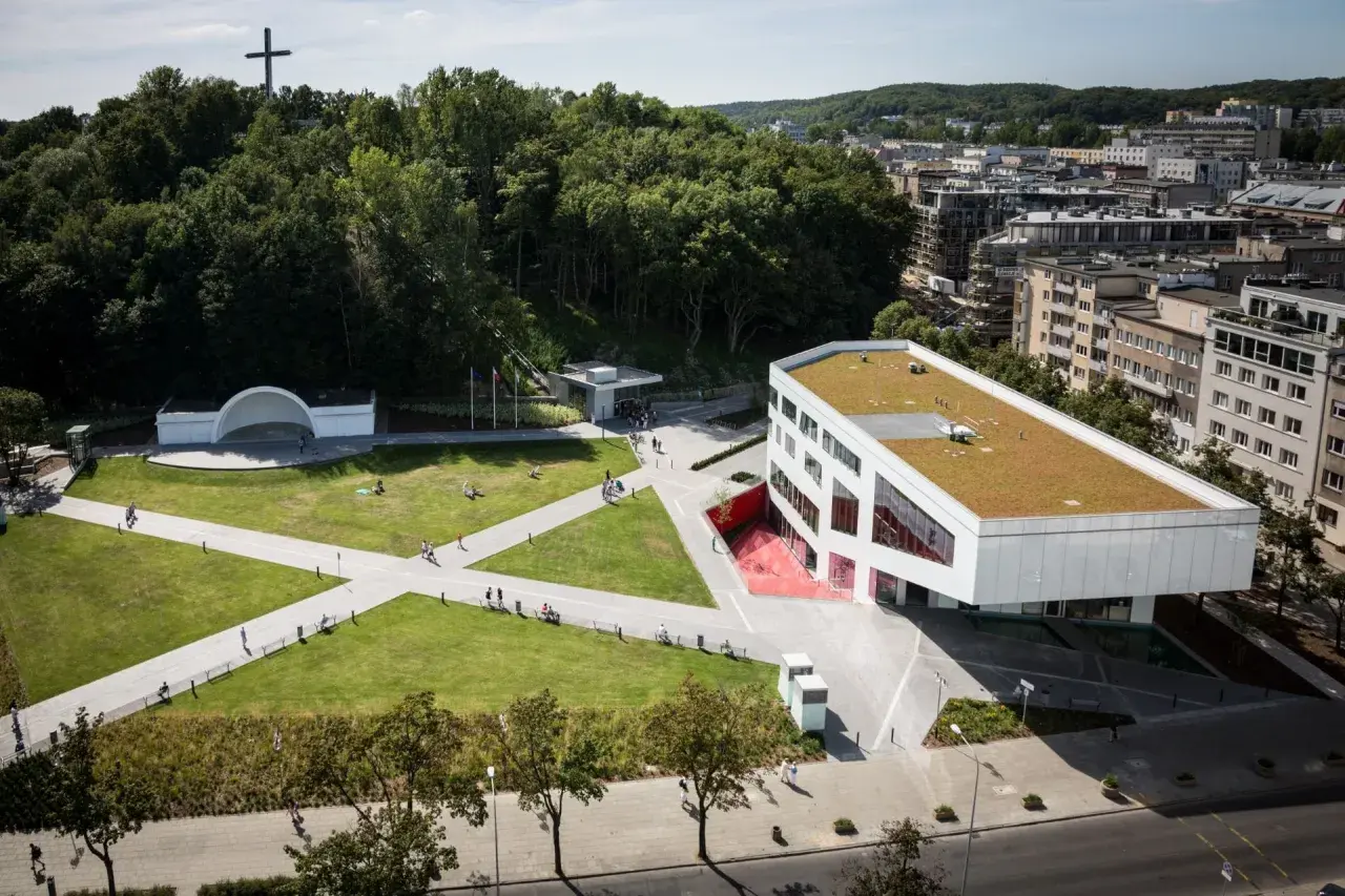 Nowoczesny budynek Gdyńskiego Centrum Filmowego z zielonym dachem, otoczony parkiem z amfiteatrem i krzyżem na wzgórzu.