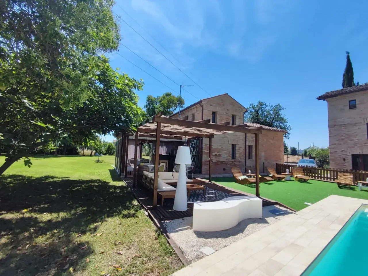 Un'oasi di relax a Poggio San Romualdo: piscina, prato verde, pergolato con divani e lettini prendisole.