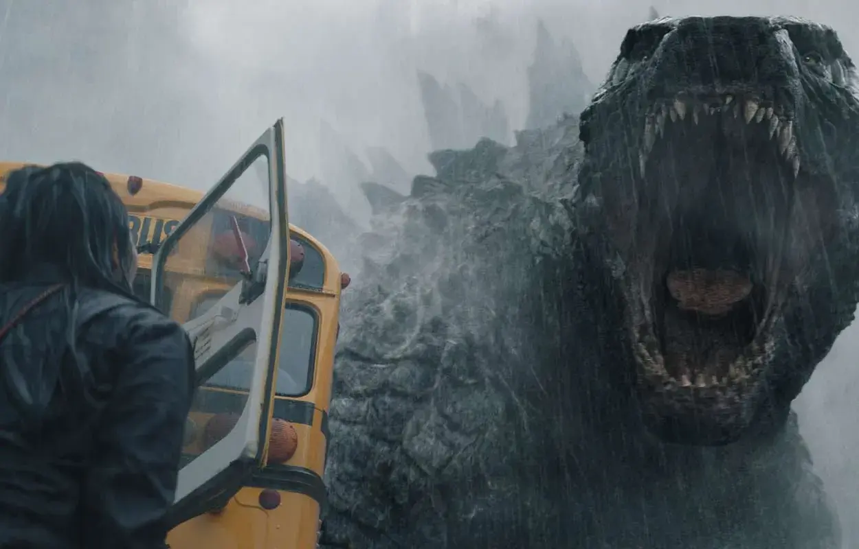 Enorm Godzilla vrålar mot en gul skolbuss i regnet, en del av **Monarch Legacy of Monsters**.