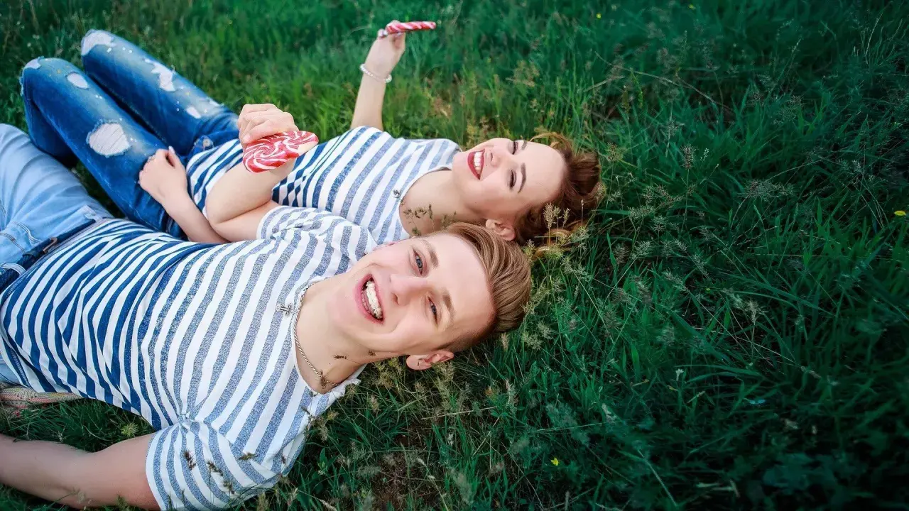 Para, która leży na trawie, trzymając lizaki. Ich uśmiechy sugerują, że mają otwarty związek, co to znaczy?